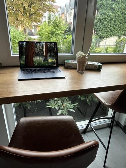 Midnight blue MacBook Air on a nice kitchen window next to a hot chocolate and cookies looking out into the green neighbourhood