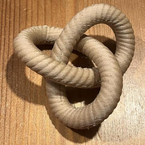 3D printed trefoil knot out of wood pla lying on a wooden table.